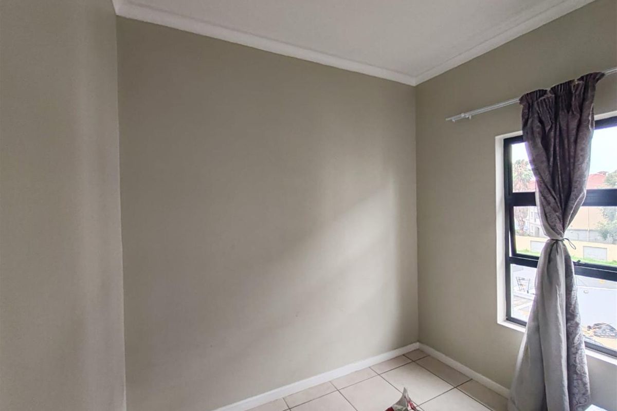 A simple bedroom featuring neutral wall paint, tiled flooring, and a window with curtain rod.