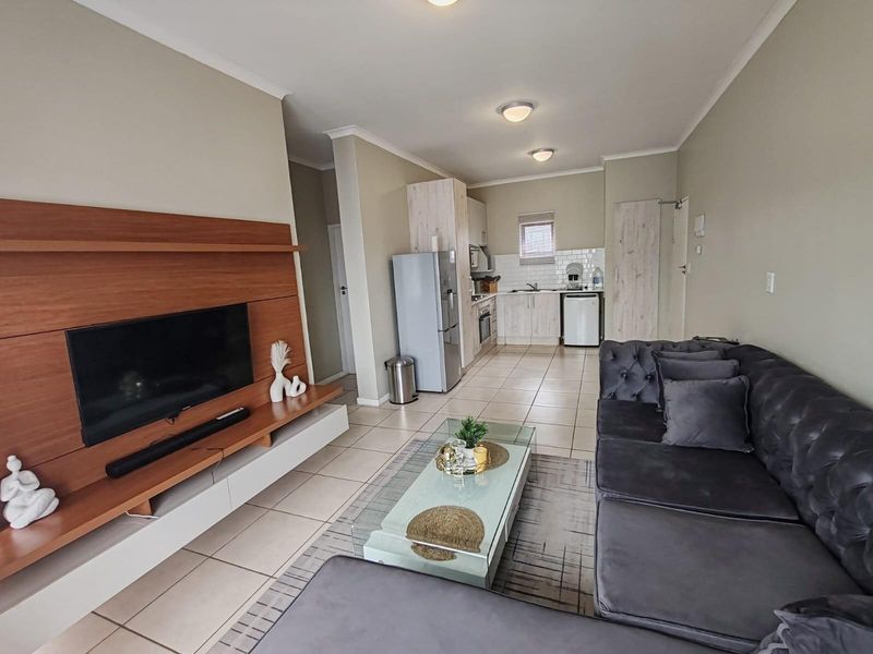 Open-plan living area featuring a modern kitchen with built-in cabinetry and tiled flooring, seamlessly flowing into a comfortable lounge space.