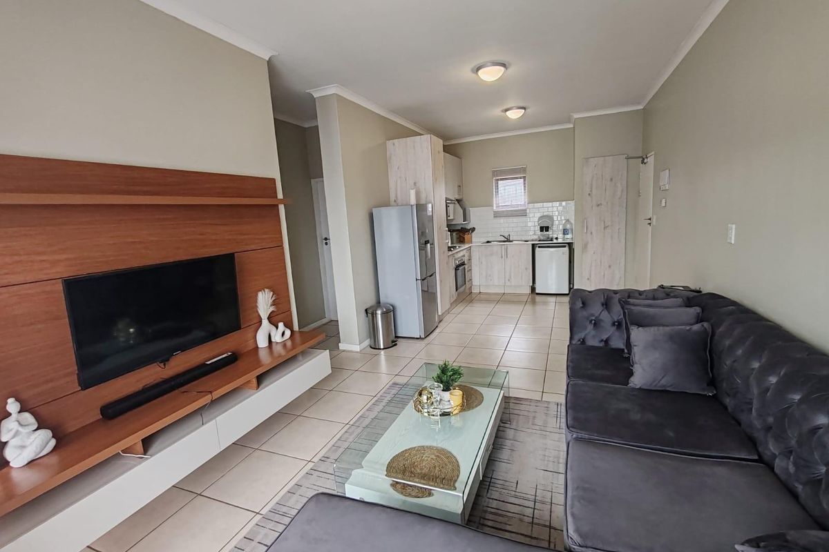 Open-plan living area featuring a modern kitchen with built-in cabinetry and tiled flooring, seamlessly flowing into a comfortable lounge space.