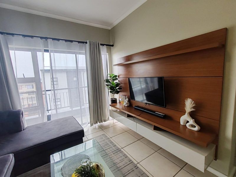 A bright living room featuring a large built-in wooden media console and sliding glass doors leading to a balcony.