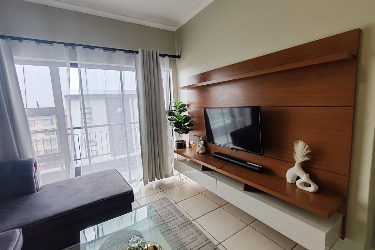 A bright living room featuring a large built-in wooden media console and sliding glass doors leading to a balcony.