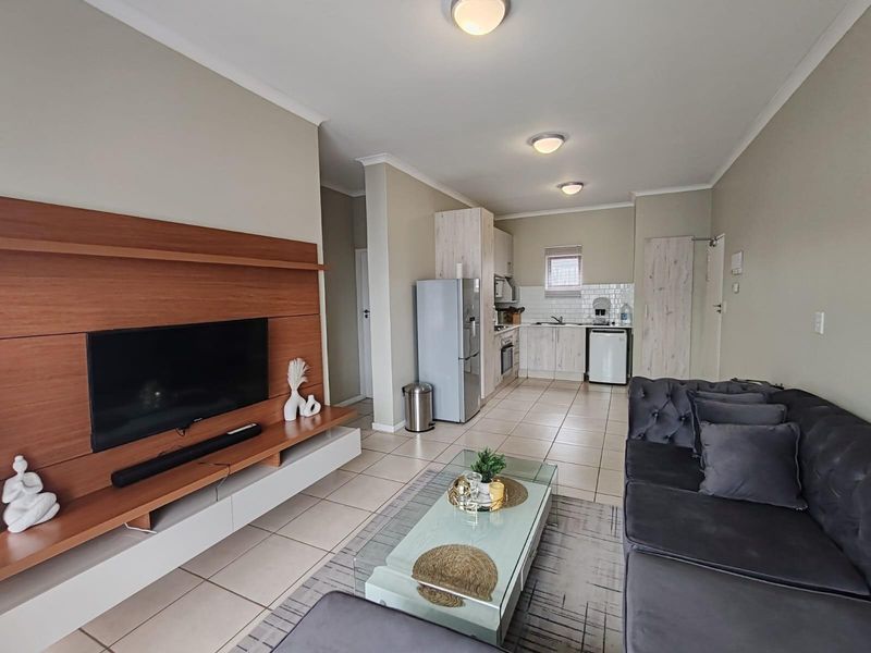 An open-plan living area featuring a modern kitchen with light wood cabinetry, tiled flooring, and a built-in media unit.