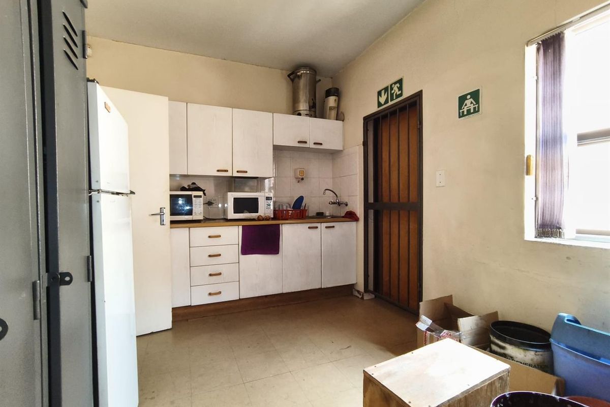 A functional office kitchenette featuring white cabinetry, a stainless steel sink, and tiled flooring, providing essential utility space for staff.