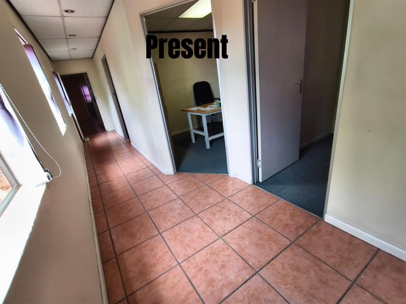 A functional office hallway featuring terracotta-style floor tiles, recessed ceiling lighting, and access to multiple individual office rooms with carpeted flooring.