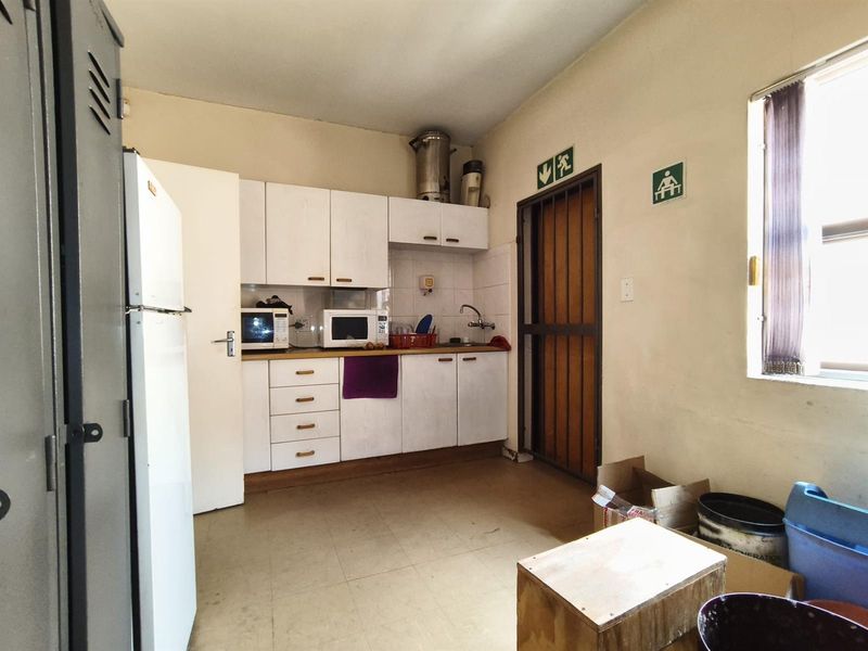 A functional office kitchenette featuring white cabinetry, a stainless steel sink, and tiled flooring, providing essential utility space for staff.