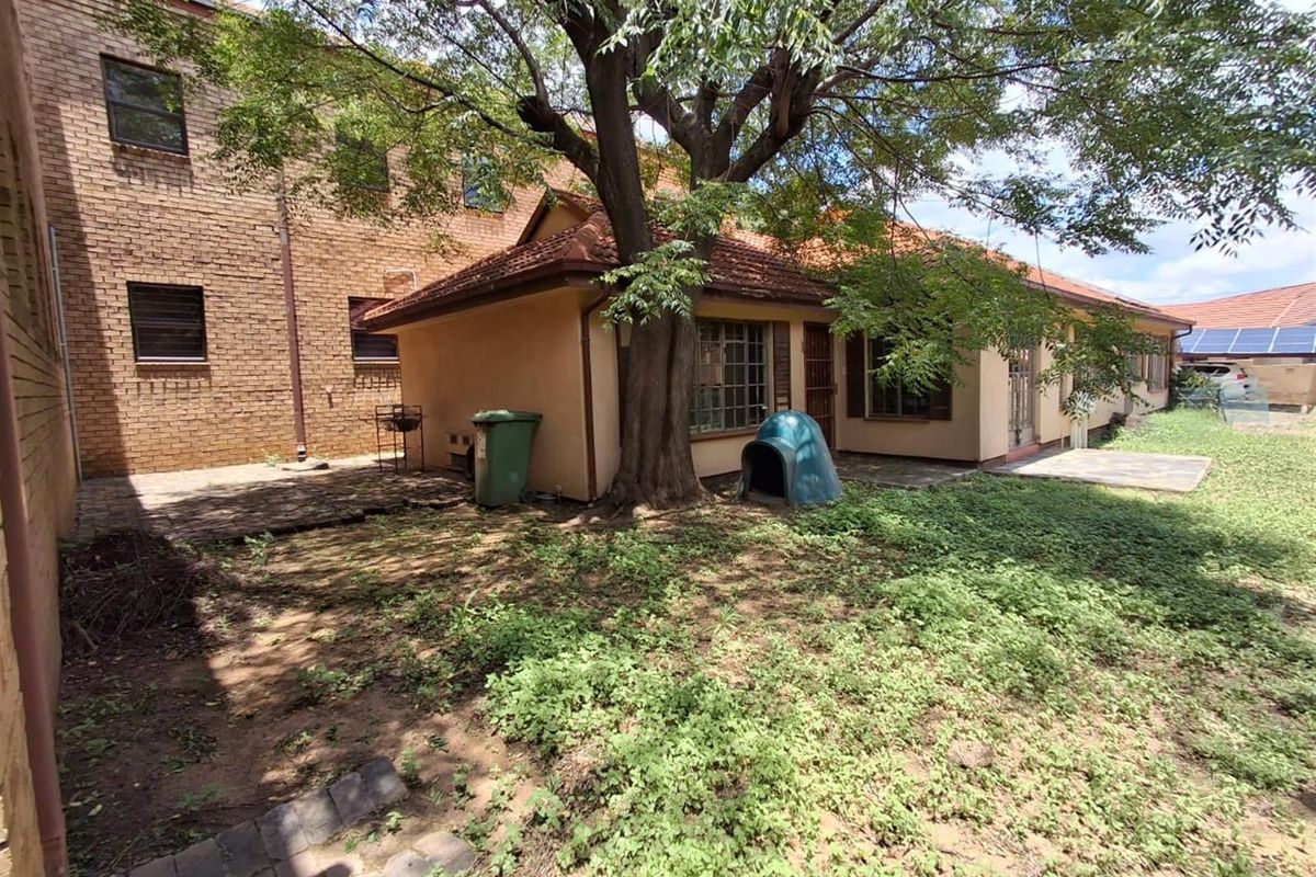 Rear view of the office property featuring a paved patio area, mature tree, and established garden space.