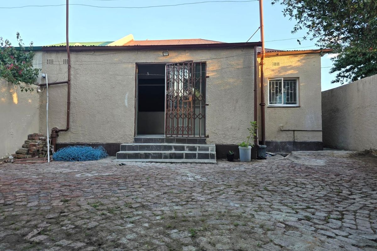 Rear view of the property featuring a paved courtyard, security gate entrance, and exterior wall finishes.