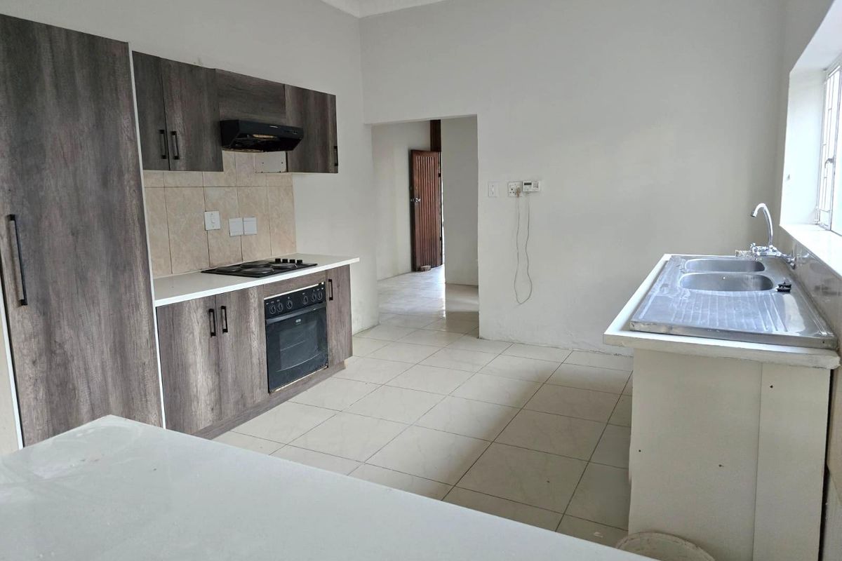 A functional kitchen featuring wood-look cabinetry, a built-in oven, hob, extractor fan, and a double stainless steel sink with tiled splashbacks.