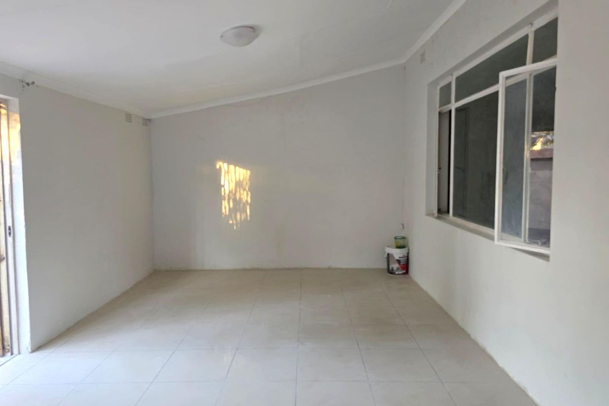 A bright, empty living room featuring neutral tiled flooring, white walls, and large windows that provide ample natural light.