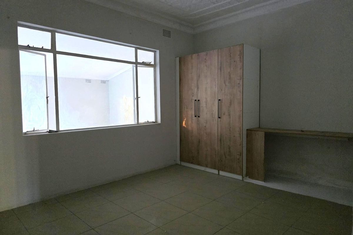 A vacant bedroom featuring tiled flooring, a built-in wooden wardrobe, and a built-in desk area with large windows providing natural light.