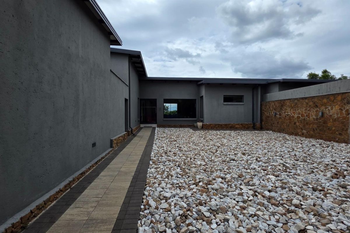 A modern exterior rear courtyard featuring a paved walkway, stone-covered ground, and textured grey walls with stone cladding accents.