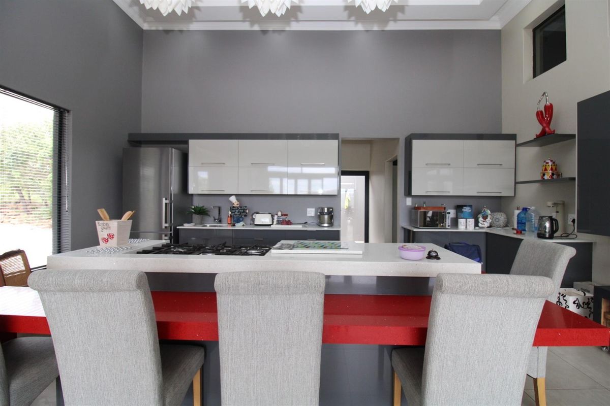 Modern kitchen featuring high-gloss cabinetry, a central island with a built-in gas hob, and stone countertops, set against a high-ceilinged grey interior.