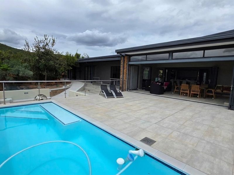 Spacious outdoor patio area featuring a swimming pool, stone-clad chimney, and large folding glass doors leading into the main living space.