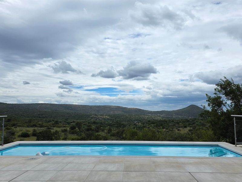 A modern swimming pool with a glass balustrade, offering expansive views of the surrounding natural landscape and hills.