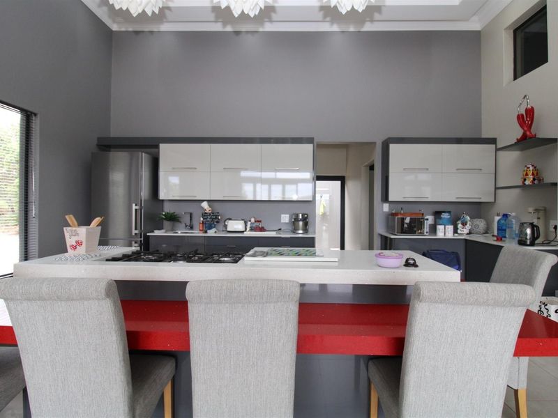 Modern kitchen featuring high-gloss cabinetry, a central island with a built-in gas hob, and stone countertops, set against a high-ceilinged grey interior.