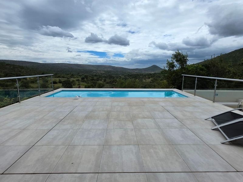 A modern outdoor pool area featuring a tiled deck, glass balustrades, and expansive views of the surrounding landscape.