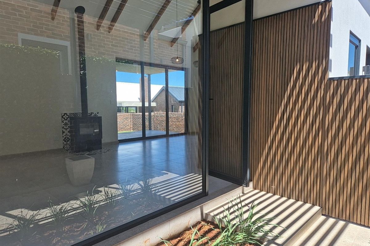 Modern living area featuring exposed timber ceiling beams, a built-in fireplace, and large glass sliding doors opening to an outdoor patio space.
