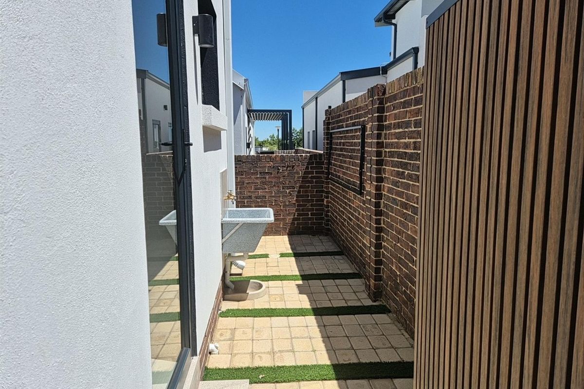 A side courtyard area featuring paved flooring with grass inserts, a brick boundary wall, and a wall-mounted utility sink.