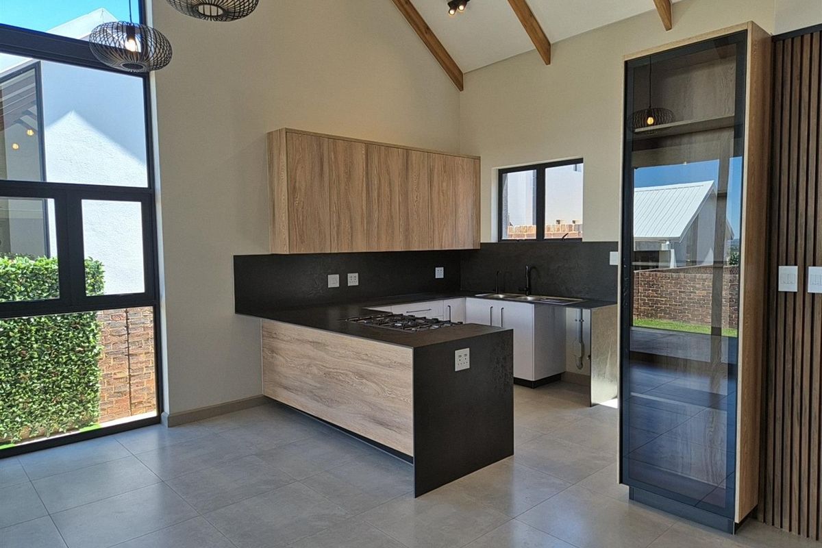 Modern kitchen featuring wood-grain cabinetry, dark stone countertops, a built-in gas hob, and high vaulted ceilings with exposed timber beams.