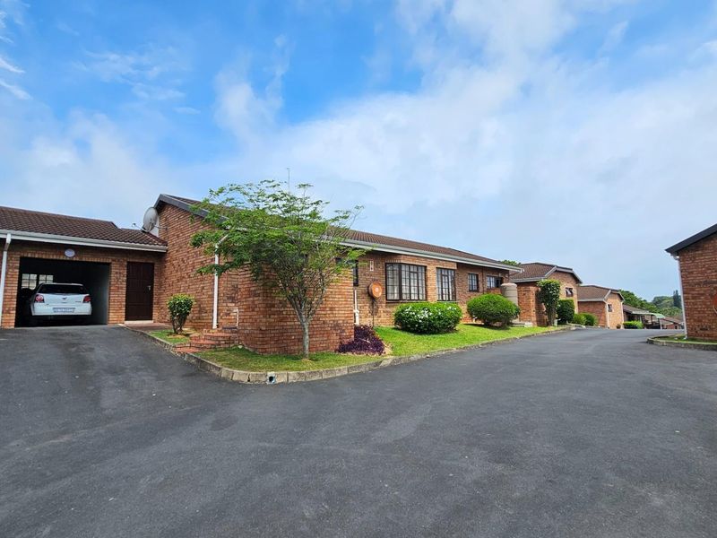 Exterior view of a brick townhouse complex featuring a paved driveway, integrated garage, and established garden beds.
