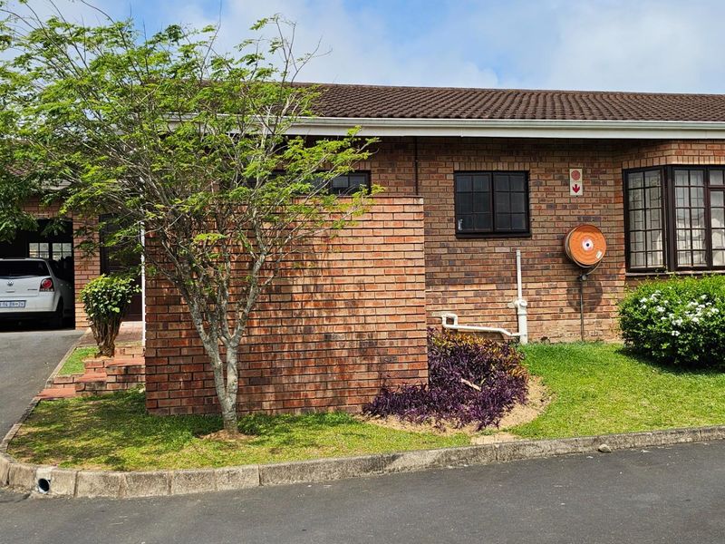 Front exterior view of a brick townhouse featuring a paved driveway, attached garage, and established garden area.