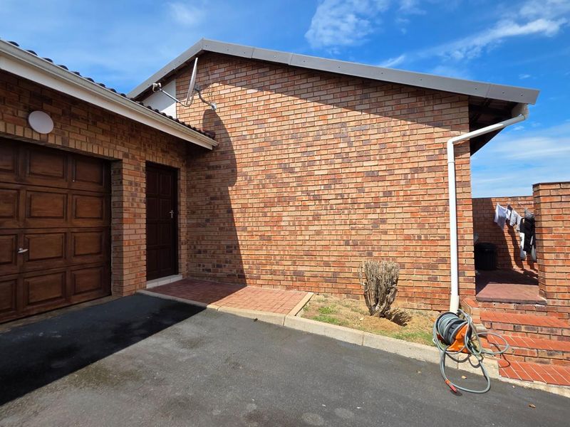Exterior view of the townhouse featuring a face-brick facade, a single garage door, and paved driveway access.