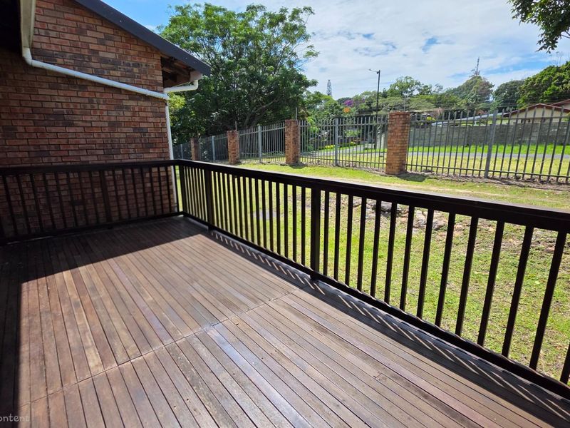 A raised timber deck patio featuring a dark wood railing, overlooking a private garden area with perimeter brick and steel fencing.