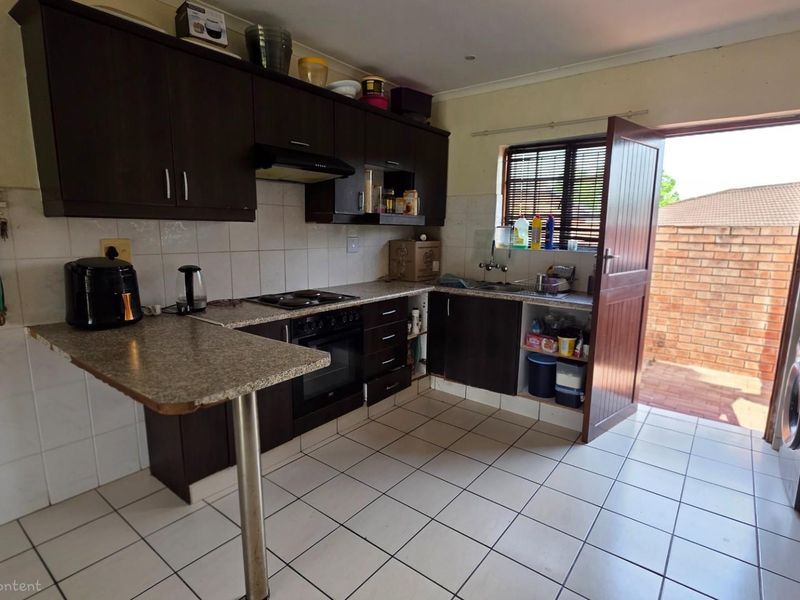 Functional kitchen featuring dark cabinetry, built-in oven and hob, tiled splashbacks, and direct access to an outdoor area.