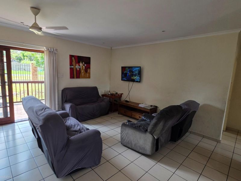 A living room featuring tiled flooring, a ceiling fan, and sliding glass doors providing access to an outdoor patio area.