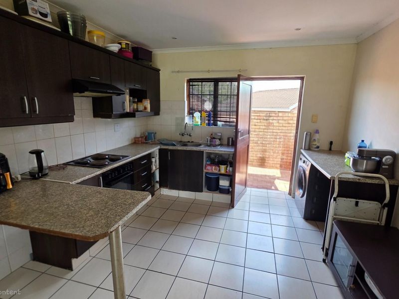Functional kitchen featuring dark cabinetry, built-in oven and hob, tiled flooring, and direct access to an exterior courtyard area.