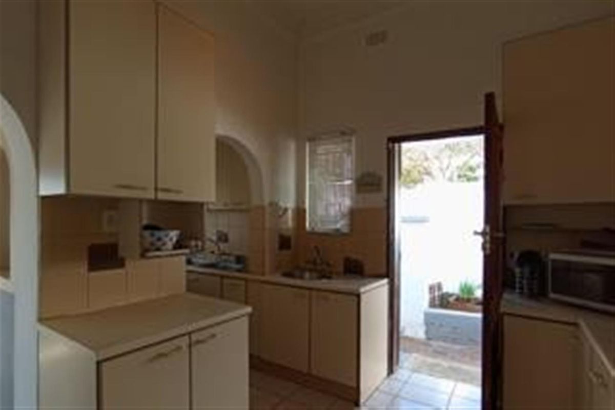 A dated kitchen featuring laminate cabinetry, tiled splashbacks, and direct access to an outdoor area.