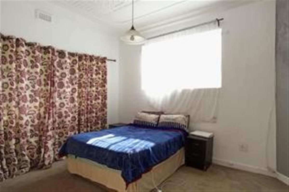 A bedroom featuring high ceilings with decorative cornicing, a large window with natural light, and neutral wall finishes.