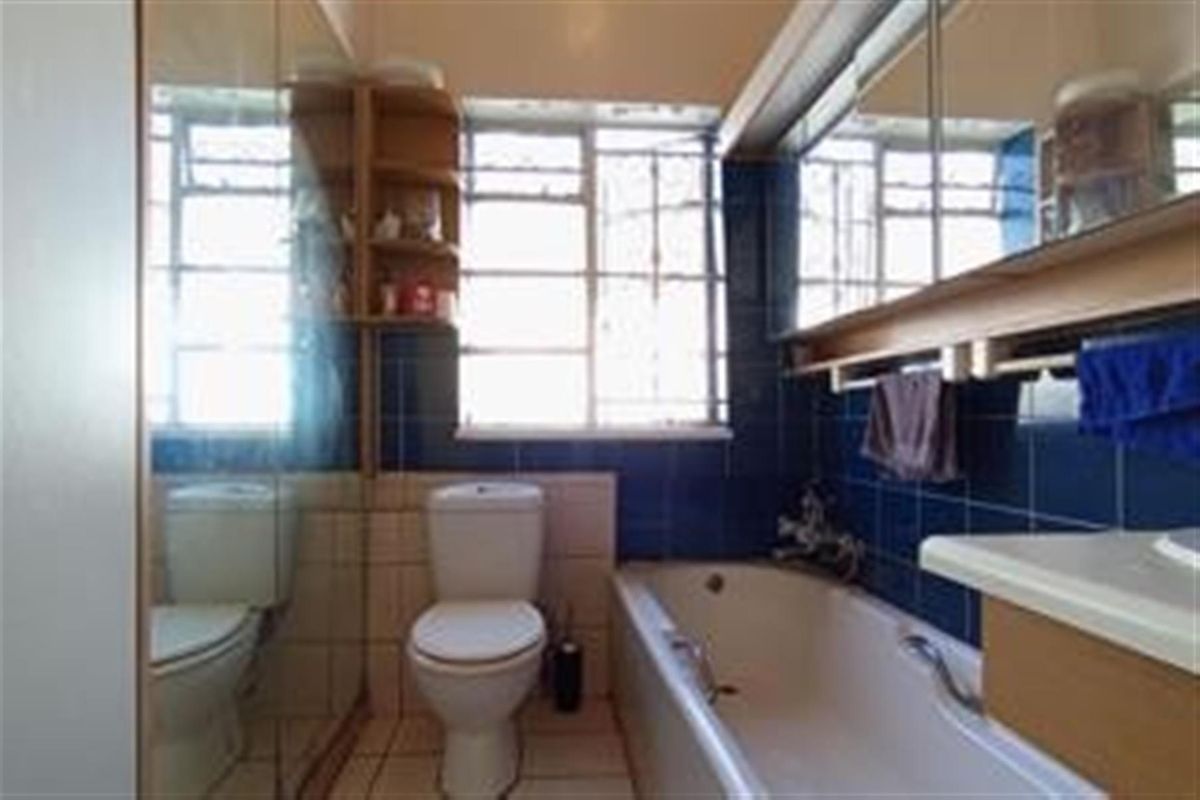 A dated bathroom featuring a standard bathtub, toilet, and vanity unit with blue wall tiles and large mirrored cabinetry.