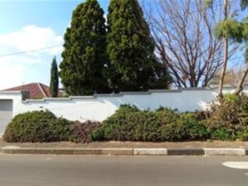 Street view of the property showing the boundary wall, mature landscaping, and garage entrance from the road.