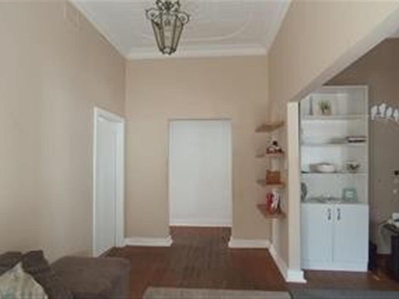 A hallway featuring hardwood flooring, built-in shelving, and a decorative ceiling rose, providing access to adjacent living spaces.