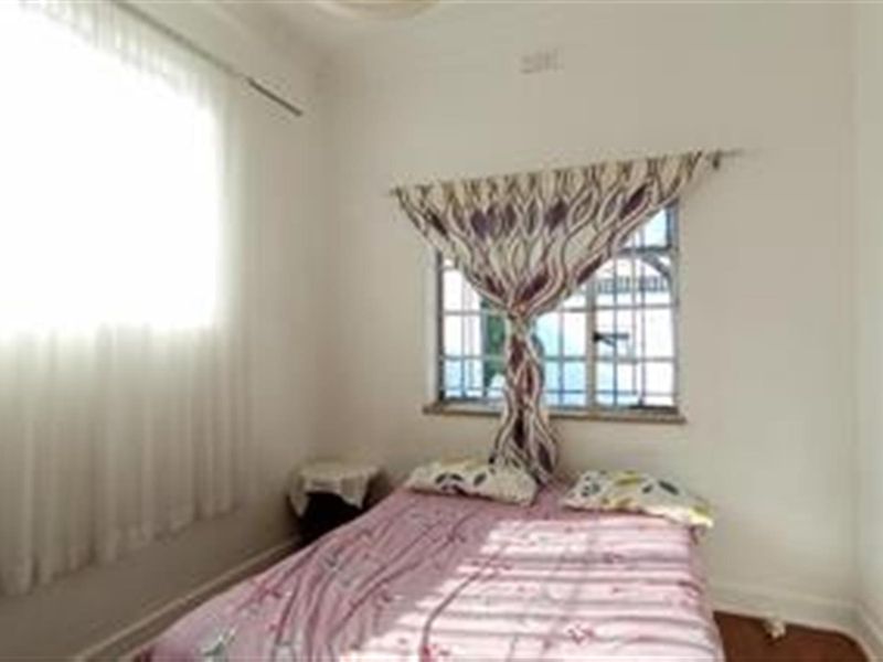 A standard bedroom featuring white walls and windows fitted with security bars.