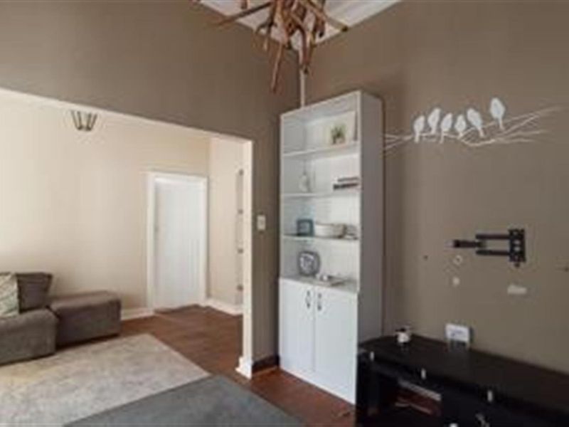 A living room area featuring hardwood flooring, a built-in storage unit, and a wall-mounted television bracket, leading into an adjacent room.