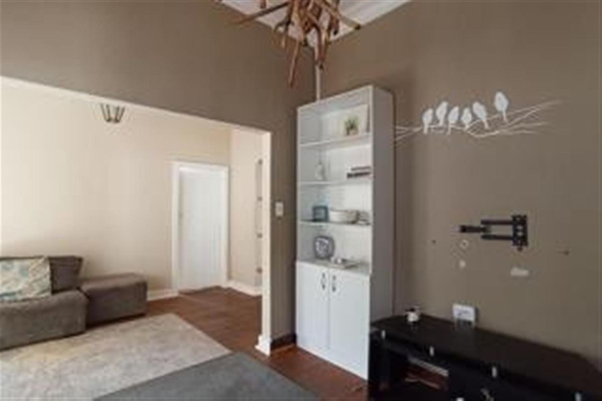 A living room area featuring hardwood flooring, a built-in storage unit, and a wall-mounted television bracket, leading into an adjacent room.