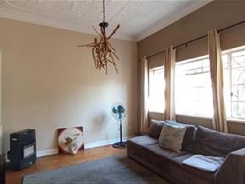 A living room featuring hardwood flooring, ornate ceiling detailing, built-in shelving, and large windows that provide ample natural light.
