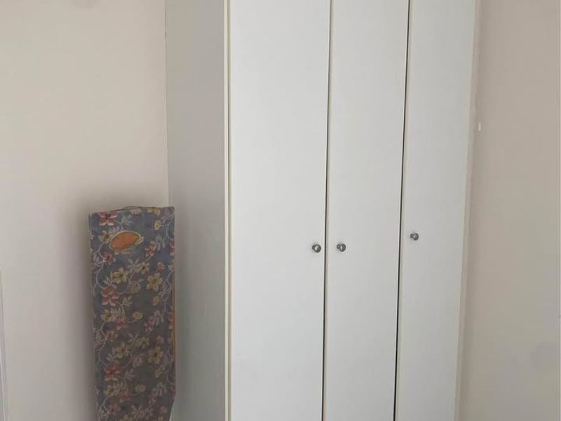 A bedroom featuring a white built-in wardrobe with three doors and decorative ceiling cornice.