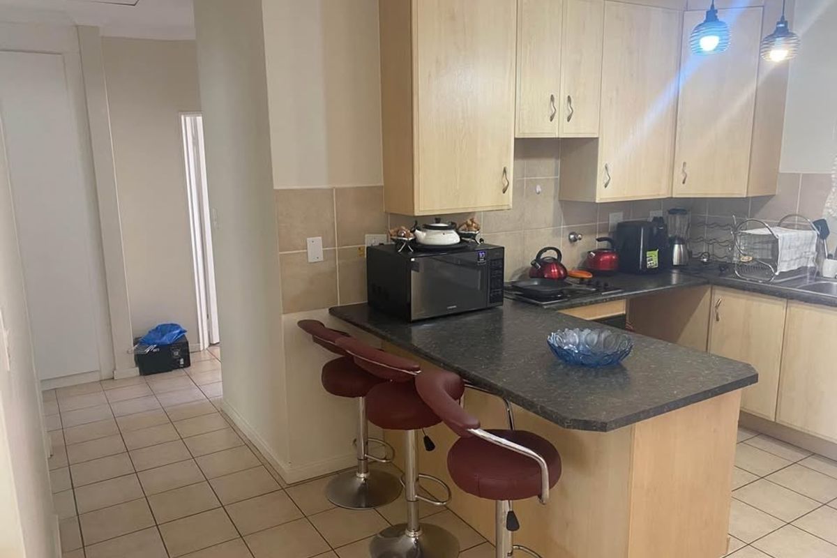 Functional kitchen featuring light wood cabinetry, dark laminate countertops, a breakfast bar, and tiled flooring, offering a practical layout for daily use.
