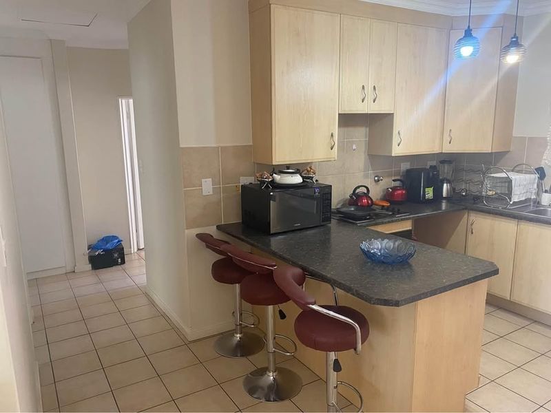 Functional kitchen featuring light wood cabinetry, dark laminate countertops, a breakfast bar, and tiled flooring, offering a practical layout for daily use.