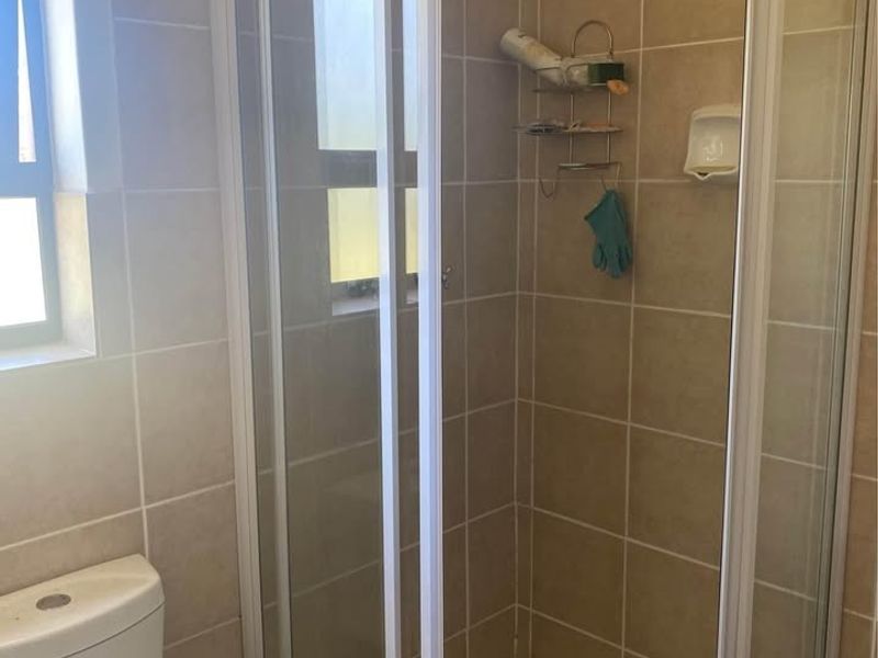 A functional bathroom featuring a corner shower enclosure with sliding glass doors, a standard toilet, and neutral wall and floor tiling.