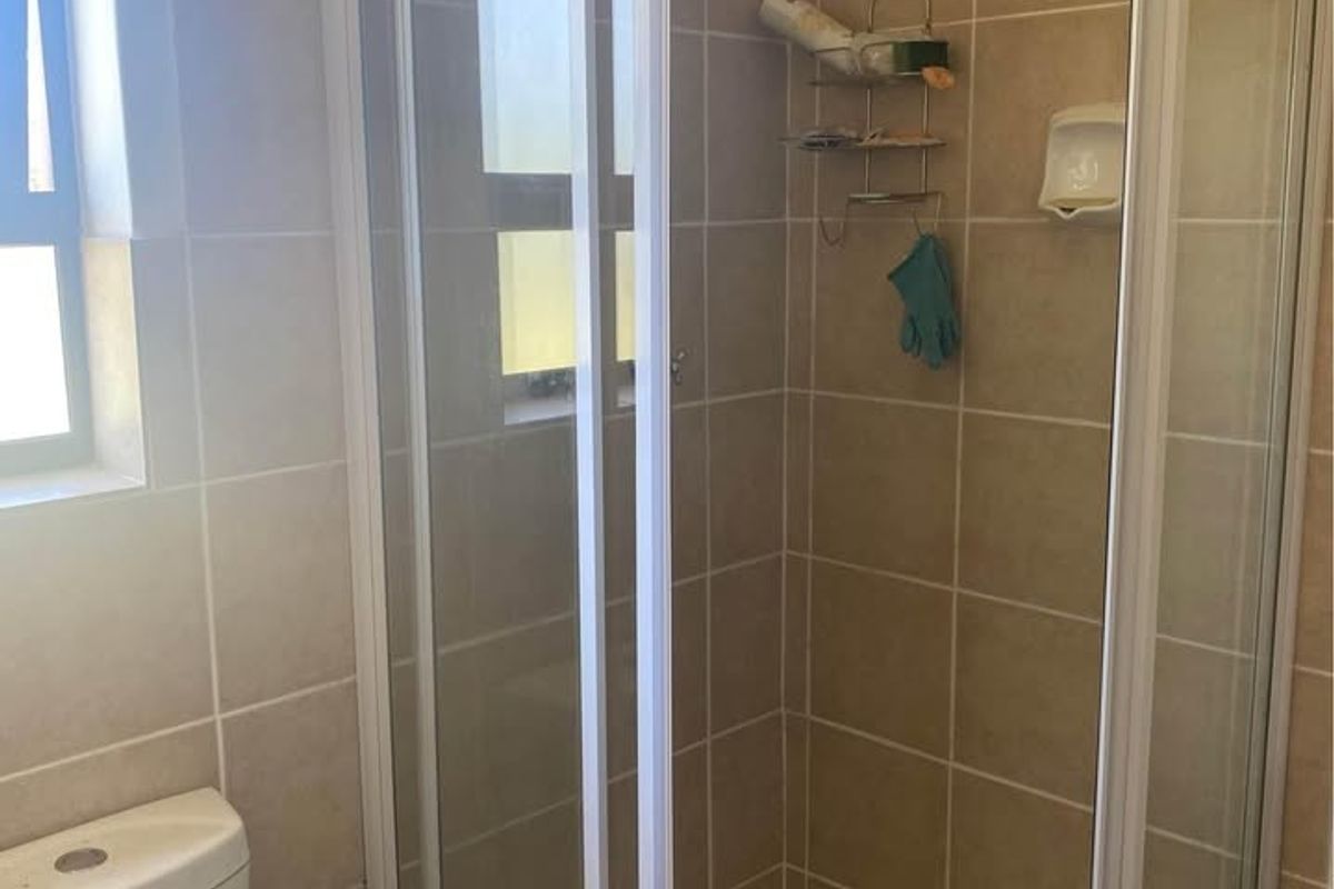 A functional bathroom featuring a corner shower enclosure with sliding glass doors, a standard toilet, and neutral wall and floor tiling.
