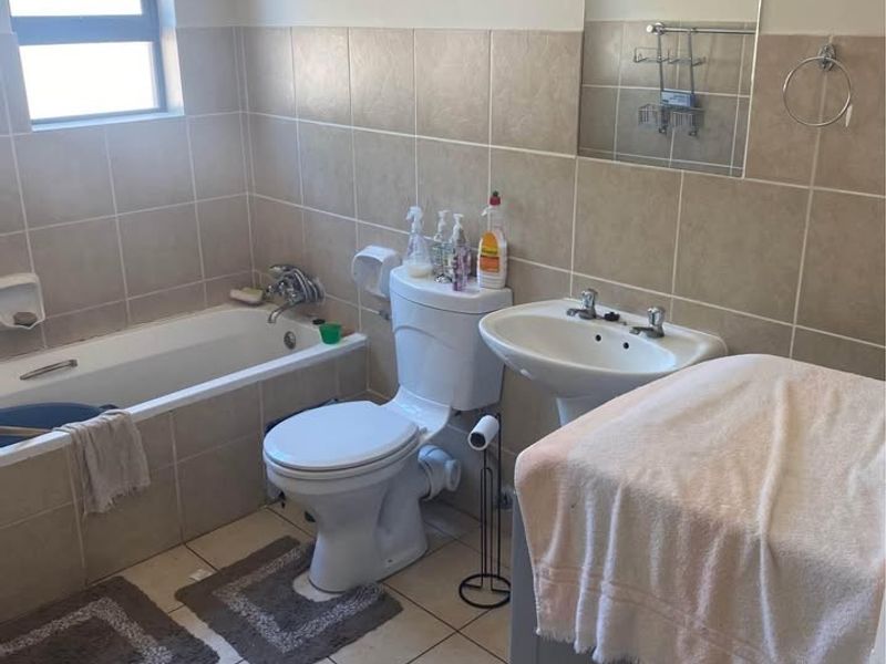 A functional bathroom featuring a bathtub, pedestal basin, and toilet with neutral wall and floor tiling.