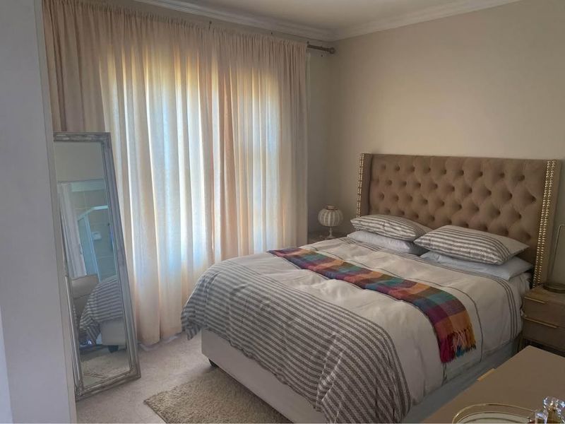 A well-maintained bedroom featuring neutral wall tones, coving, and a large window dressed with floor-length curtains.