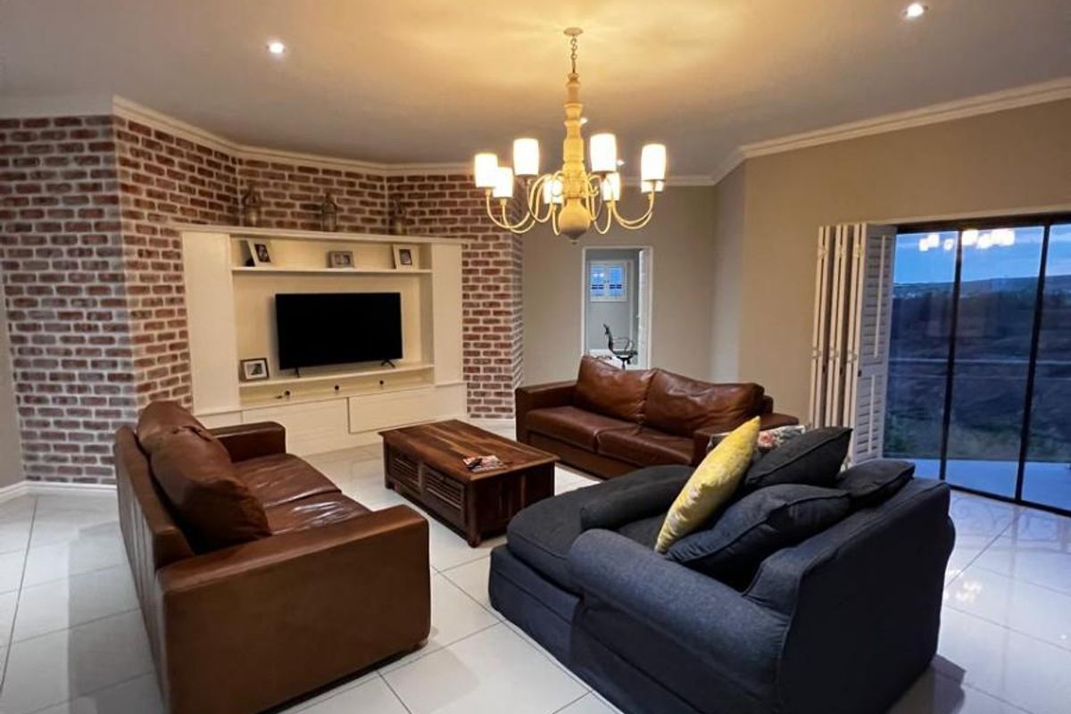 Spacious living room featuring a striking exposed brick feature wall, built-in media cabinetry, polished tiled floors, and large sliding doors leading to the exterior.