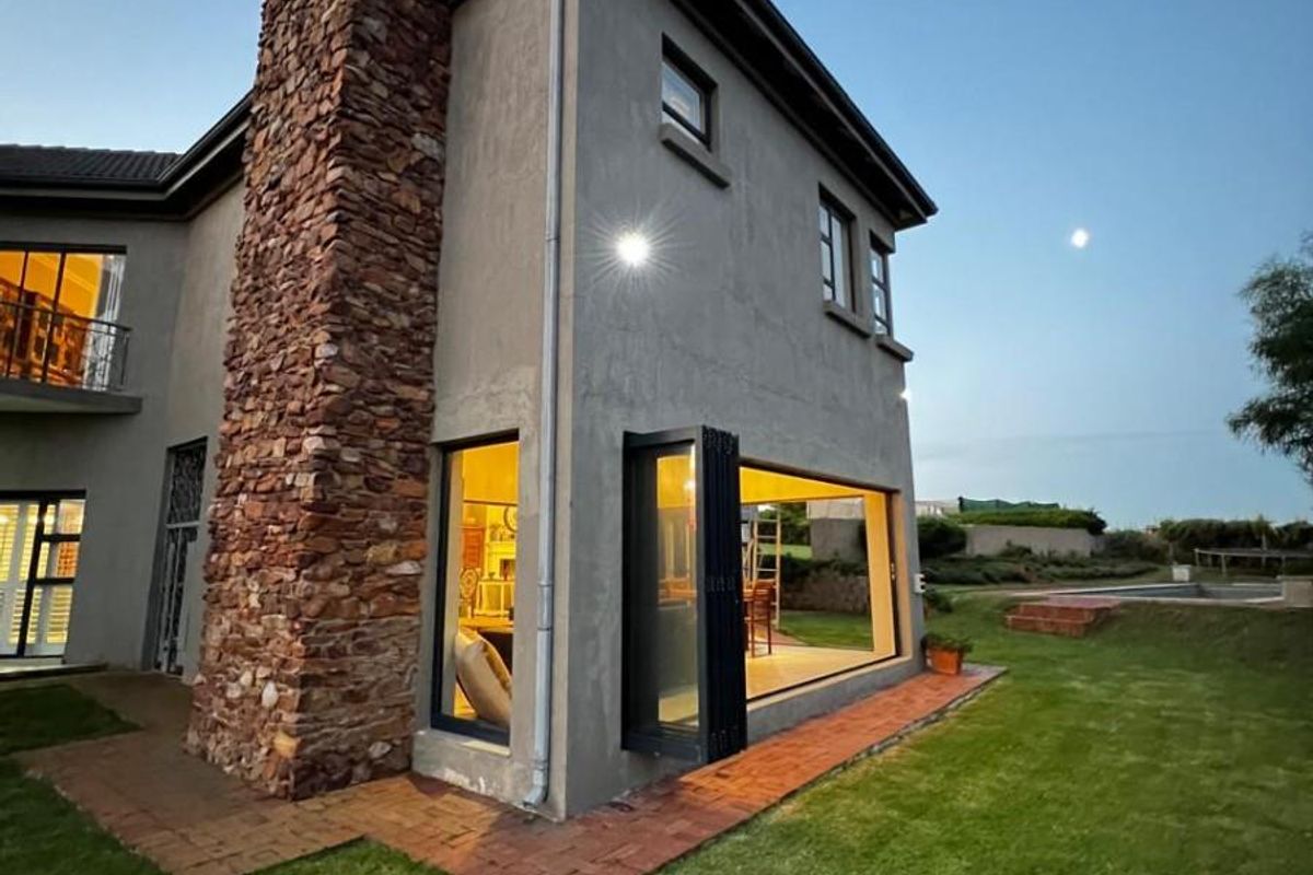 Rear view of a double-story home featuring a prominent stone chimney, modern bi-fold doors opening to the garden, and brick paved pathways.