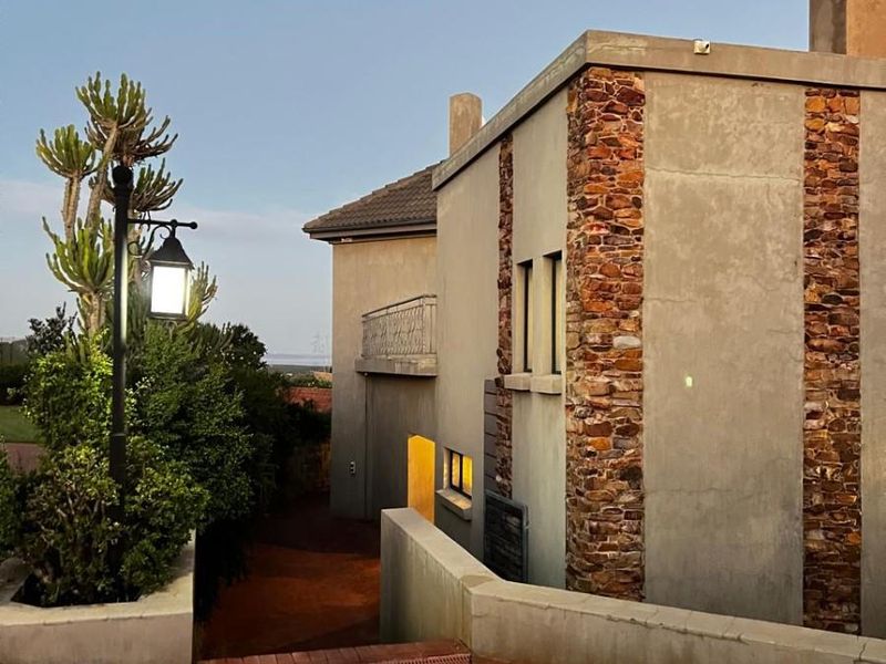 Exterior view of a small holding residence featuring stone-clad masonry walls, a brick-paved driveway, and a chimney stack at dusk.