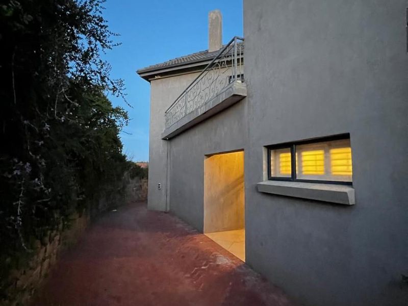 A view of the rear exterior of the property featuring a balcony with wrought iron railing and a paved pathway at dusk.